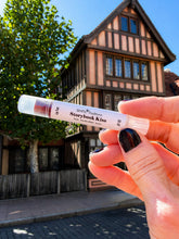 Hand holding a lip balm tube with a beauty and the beast looking building in the background